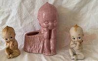 Photo of two small vintage Kewpie doll figurines flanking a pink glazed ceramic Kewpie planter on white background.
