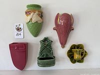 Group of five ceramic wall pockets shown hanging on wall: pale green Mulberry with white doves; pink speckled Royal Winton flower-shaped; green thatched basket with white doves; loden-colored windmill; budding yellow teacup flower.