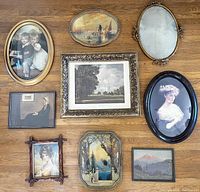 Top-down photo of all nine framed artworks and frames arranged on a hardwood floor, showing variety of sizes, frame materials, and glass coverage