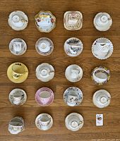 Overview of 19 assorted patterned teacups and matching saucers arranged on a wooden surface, showing diverse styles and shapes.