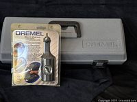 Closed grey hard plastic Dremel case next to original packaged Dremel electric engraver attachment