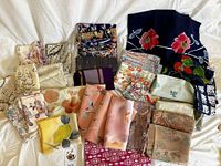 Full view of the mixed lot of folded silk fabrics showcasing various colors and patterns including dark blue with floral designs, multicolor florals, and pastel peach and cream fabric pieces