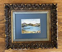 Framed original watercolor landscape showing the full ornate carved wood frame with gilt finish and blue matting.