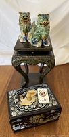 Pair of glazed ceramic Foo dogs on pedestal and black lacquer box with inlay on wooden floor