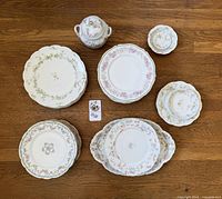 Overhead photo of multiple mixed patterned Haviland plates and a lidded sugar bowl arranged on wooden floor.