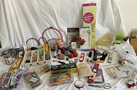 Full overview of sewing notions and supplies spread on table, showing spools of thread, embroidery floss, scissors, pincushions, measuring tapes, pattern rulers, and various sewing tools.