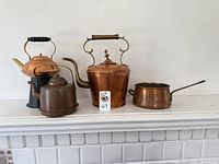 Front view of all four items on a white shelf including three kettles and one saucepan showing shapes and colors