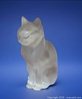 Full view of the Lalique Minette sitting cat figurine on a blue background showing frosted and clear crystal texture.
