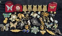 Overview of 40 vintage brooches, pins and earring sets arranged on black cloth