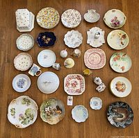 Top-down image showing a large assortment of over 30 china pieces arranged on a wooden floor, featuring varied patterns including floral and classic designs of different shapes and sizes.
