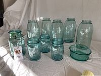 Full lot of nine vintage glass pieces displayed on white cloth, showing five pint jars, three quart jars, and one bowl without lids.