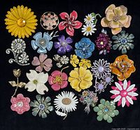 Full lot of 25+ colorful vintage floral brooches and earrings laid out on black fabric showing variety of enamel, rhinestone, metal and resin flowers in multiple colors and styles.