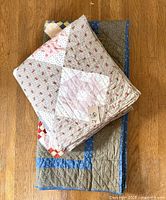 Stacked view showing two folded handmade quilts, blue-framed Amish-style quilt bottom, earth-tone patchwork quilt top