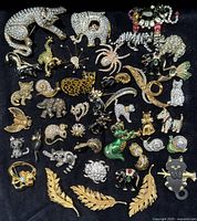 Full lot display of over 45 vintage animal-themed brooches and pins arranged on black fabric. Shows a variety of animals including rhinoceros, elephant, scorpion, spider, cat, dog, and more, featuring rhinestones, enamel, and gold-tone finishes.