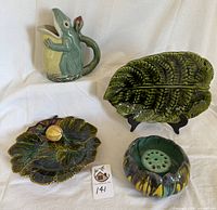 Four ceramic pieces displayed together: frog pitcher, pumpkin-form vase with insert, Steidl leaf plate with apple and vine, Sarreguemines leaf platter