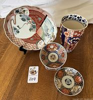 Full group of four Japanese Imari porcelain pieces: vase, scalloped plate, and two small bowls, all hand-painted with traditional motifs in red, blue and gold.