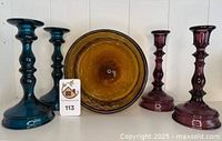 Photo showing entire lot including amber glass swirl bowl and four candlesticks in teal and amethyst colors, all with smooth curves and rich saturation.