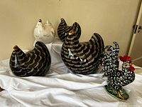 Four ceramic hens and porcelain rooster displayed on white cloth, front view