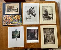 Seven vintage and contemporary art prints arranged on a wooden table, showing various styles and sizes.