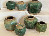 Front and top view of the seven vintage Chinese green stoneware jars showing embossed designs and glaze variation.