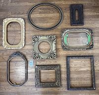 Overview of 8 different vintage and antique frames on wood floor, various shapes and finishes including gilded, carved, and painted accents.
