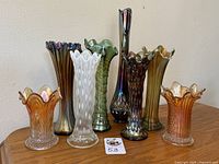 Group shot of eight carnival glass vases on wood surface, showing full set.