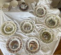 Top-down view showing all eight Royal Doulton Brambly Hedge plates arranged in a flat layout with the floral chintz creamer, sugar bowl, mini pitcher and underplate grouped at the top left.
