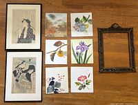 Overview of entire lot showing two framed Japanese woodblock print reproductions, six unframed watercolor-style prints on stiff board, and one ornate vintage Italian frame on wood floor.