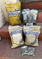 Full view of the gardening supplies on steps showing unopened bags of potting soil, pumice, decorative rock and the sealed plant hangers.