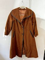 Brown mid-century coat with black piping on collar and pockets, hanging on a hanger