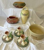 Group photo showing six pieces: pink Columbine jardiniere, ivory La Rose wall pocket, three Iris candleholders in pastel colors, tan Kitty feeder dish