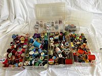 Top-down view showing numerous colorful vintage thread spools on wooden and plastic spools in clear plastic storage drawers. Spools show various brands and thread types.