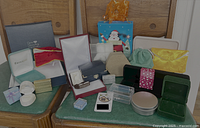 Wide variety of jewelry boxes and pouches including velvet-lined boxes, gift bags, and small ring boxes displayed on green bench