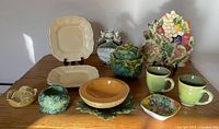 Overview of the 12 colorful ceramic and pottery pieces including serving trays, cups, bowls, and decorative items arranged on a wooden table.