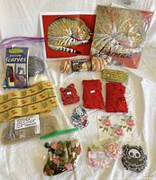 Full lot with needlepoint kit, knitting booklet and yarn, embroidery floss, patches, appliqués, and trim spread on cloth background