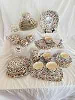 Full display of the 55-piece Royal Winton Cottage Chintz collection including teapot, cups, saucers, plates, bowls, and serving pieces with floral pattern.