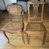 Front view of two vintage chairs, one with curved legs and arched cane backrest, the other with straight legs and ornate carved backrest.