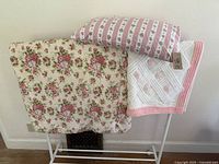 Rosebud down comforter, down rosebud patterned pillow, and chenille blanket laid over rack for display.