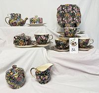 Overall view of the collection showing multiple pieces including teapot, cups, saucers, plates, creamer, butter dish, and sugar bowl with covers, all decorated in the Royal Winton Nantwich floral pattern on black background.