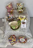 Top view of 5 Royal Winton sugar and creamer sets arranged on a lace cloth revealing brightly colored floral patterns.