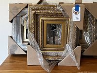 Five decorative frames in original packaging with corner protectors and plastic wrapping. Frames have rich carved decorative patterns in gold and silver finishes.
