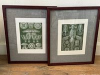 Two vintage jellyfish prints in dark wood frames leaning against a white wall on hardwood floor.