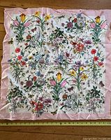 Full view of the Gucci Flora scarf showing floral pattern and pink border with measuring tape for size reference.