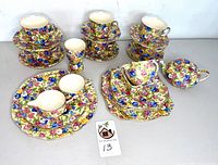 Overall view of three stacks of cups and saucers, bud vase, round serving platter with creamer and sugar, stack of square plates and teapot with lid