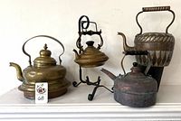 Four vintage tea kettles arranged on a white surface, showing various designs, sizes, and condition.