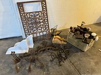Full lot showing ornate cast iron grate, wooden corbels, door knob box, wrought iron foot mounts, white shelf brackets, brass teapot, and broken wrought iron frieze on concrete floor.