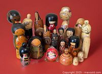Wide view of 19 wooden kokeshi dolls and red Daruma doll arranged on red background