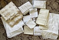 Overall view of collection showing folded vintage linens with crochet, embroidery, and lace trims on patterned surface.