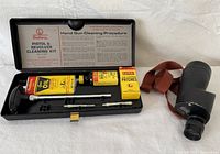 Outers handgun cleaning kit open showing all cleaning components in a black hard case with cleaning instructions on inside of lid and Mayflower monocular strap visible.