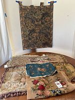 Photo showing large vintage tapestry wall hanging with hanging tabs and tapestry pillow covers laid out on table.